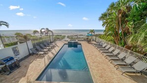Un espace piscine avec des chaises longues, un barbecue et une vue sur la plage.