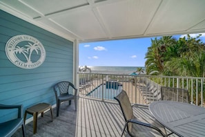 A balcony with a view of the ocean, a palm tree, and a sign that reads 'Welcome to Four Shores Palm Condo.'