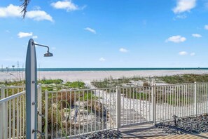 A beach view with a metal fence, a wooden deck, and a metal structure, possibly a shower, overlooking the ocean.
