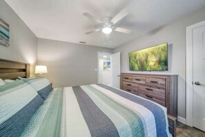 Um quarto com uma cama, um ventilador de teto, uma cômoda e uma televisão na parede.