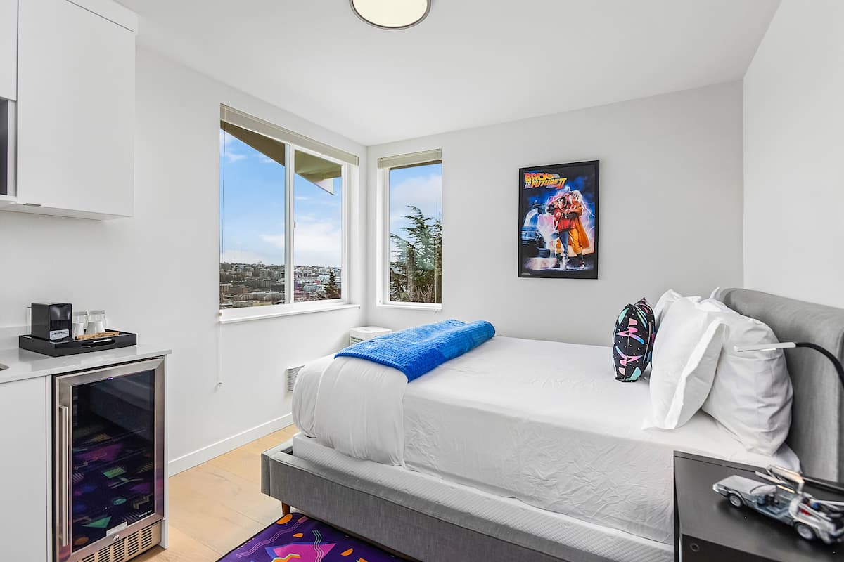 A modern bedroom with a bed, a coffee machine, a refrigerator, and a city view.