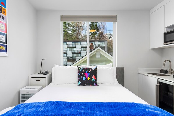 A modern hotel room with a large bed, a small kitchenette, and a window with a view of buildings. - Back To The Future Sweet Suites (Seattle)