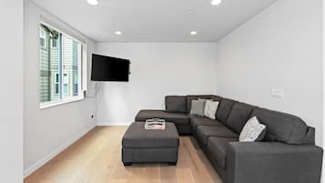 Uma sala de estar moderna com um sofá seccional, uma televisão de tela plana na parede e piso de madeira.