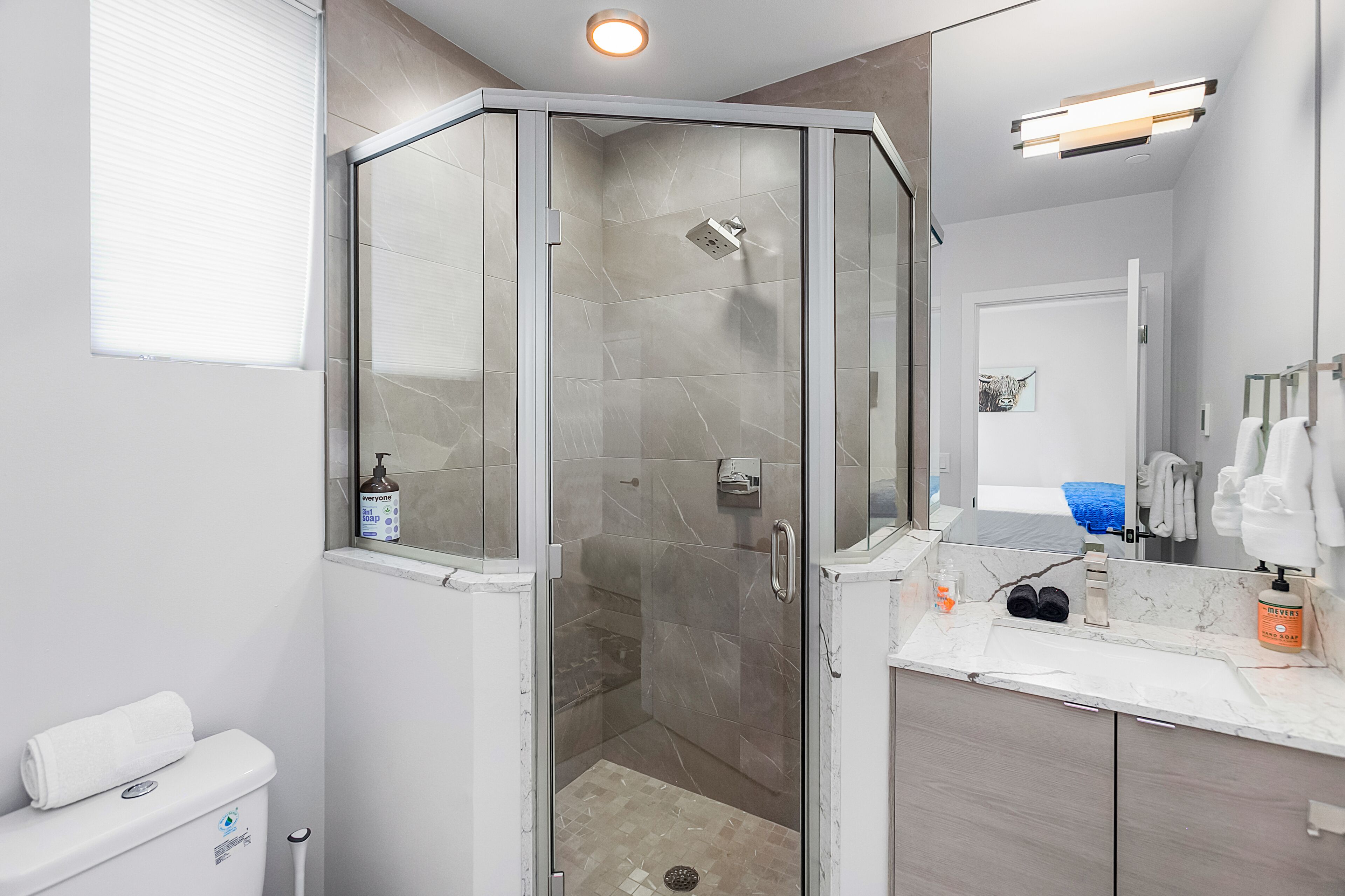 A modern bathroom with a glass-enclosed shower, a toilet, a sink with a mirror, and a towel rack.