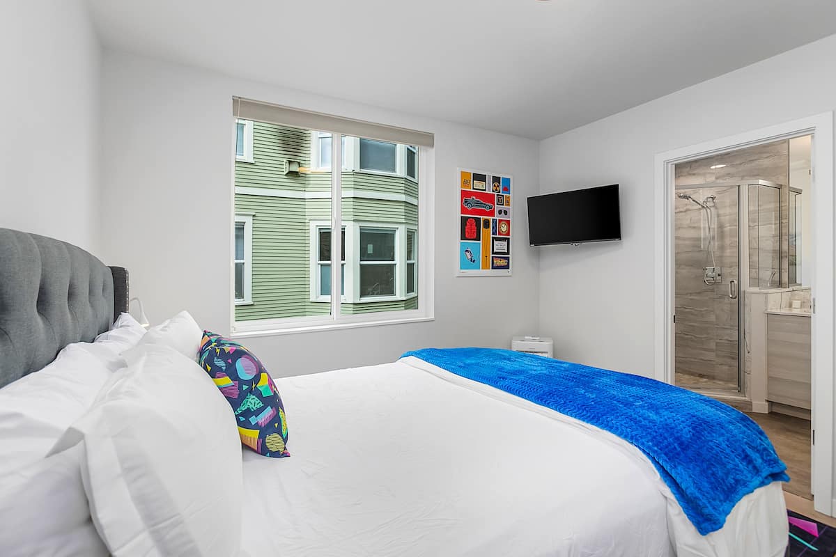 A bedroom with a bed, a window, a TV, and a shower area.