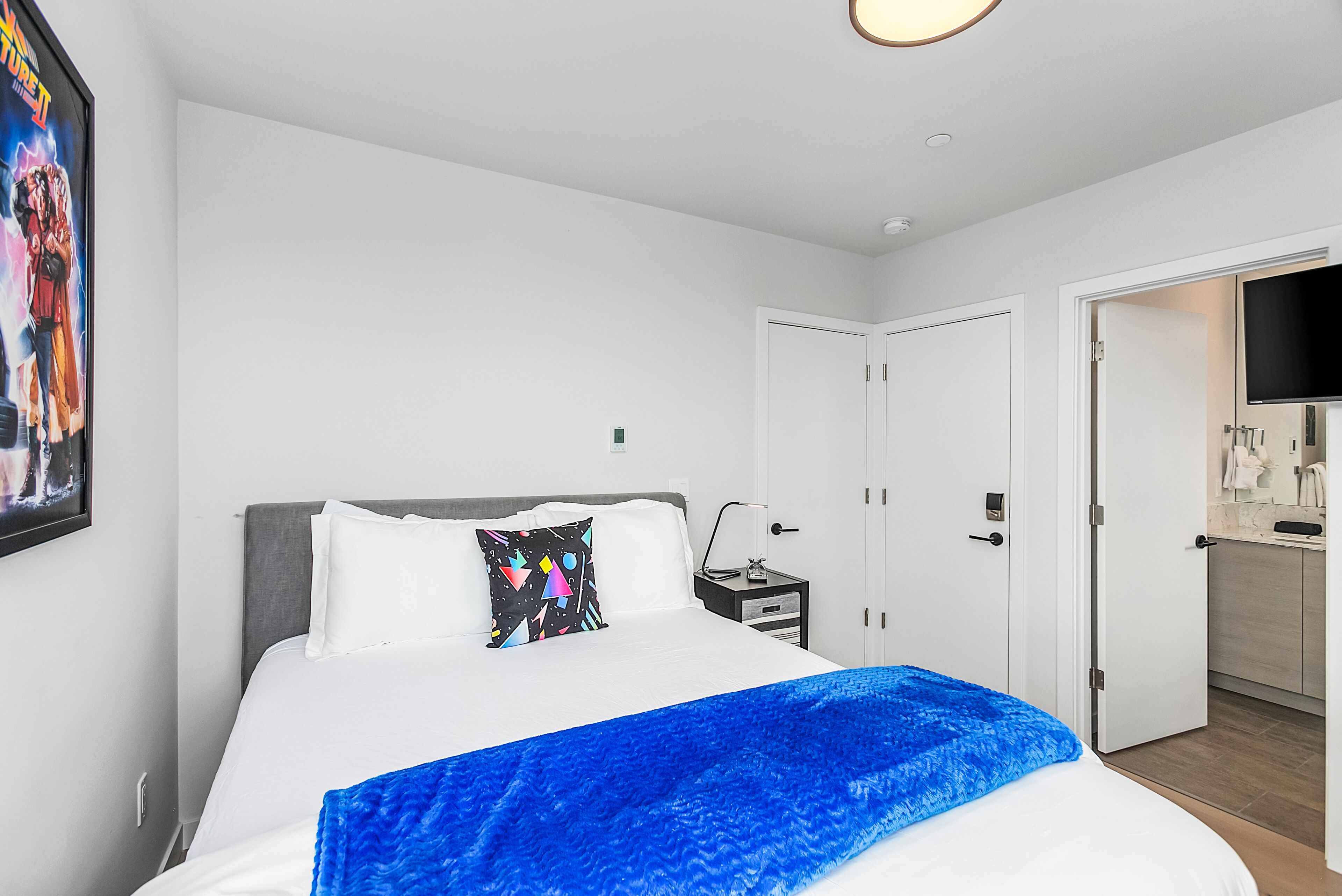 Una habitación de hotel moderna con una cama grande, una mesita de noche, un televisor y una puerta que da a un baño.
