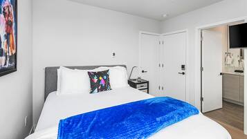 Una habitación de hotel moderna con una cama grande, una mesita de noche, un televisor y una puerta que da a un baño.