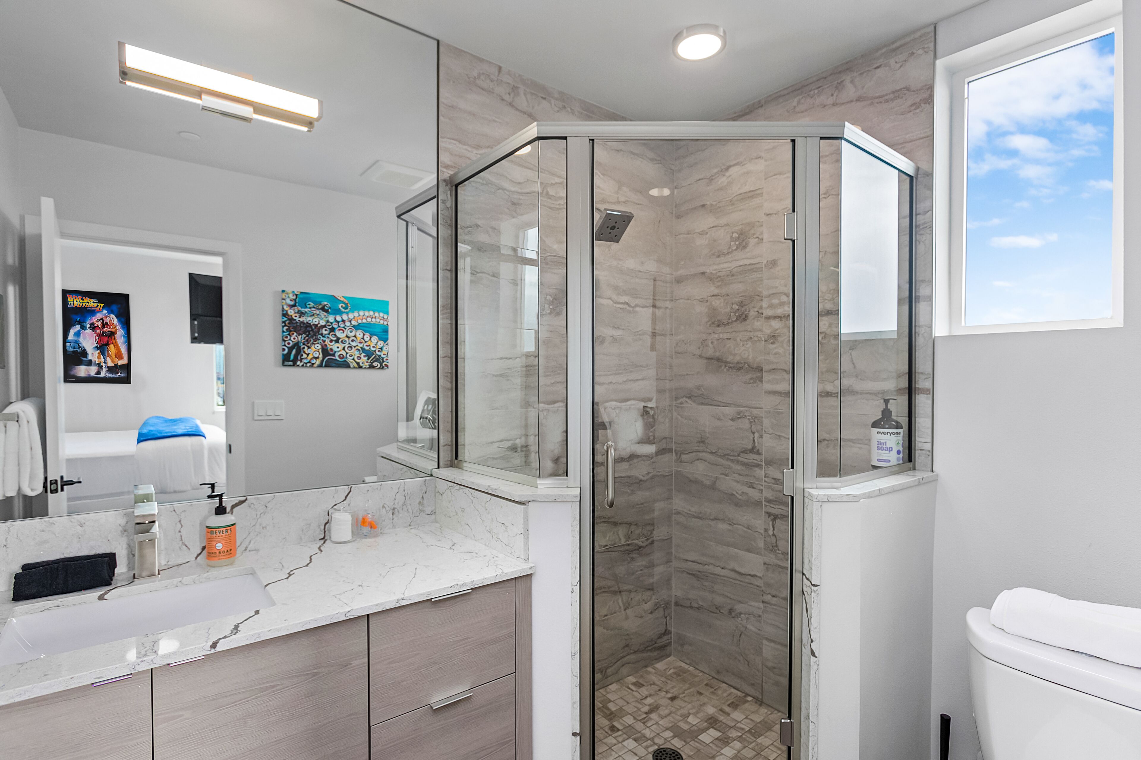 Un bagno moderno con doccia vetrata, piani di lavoro in marmo e un grande specchio.