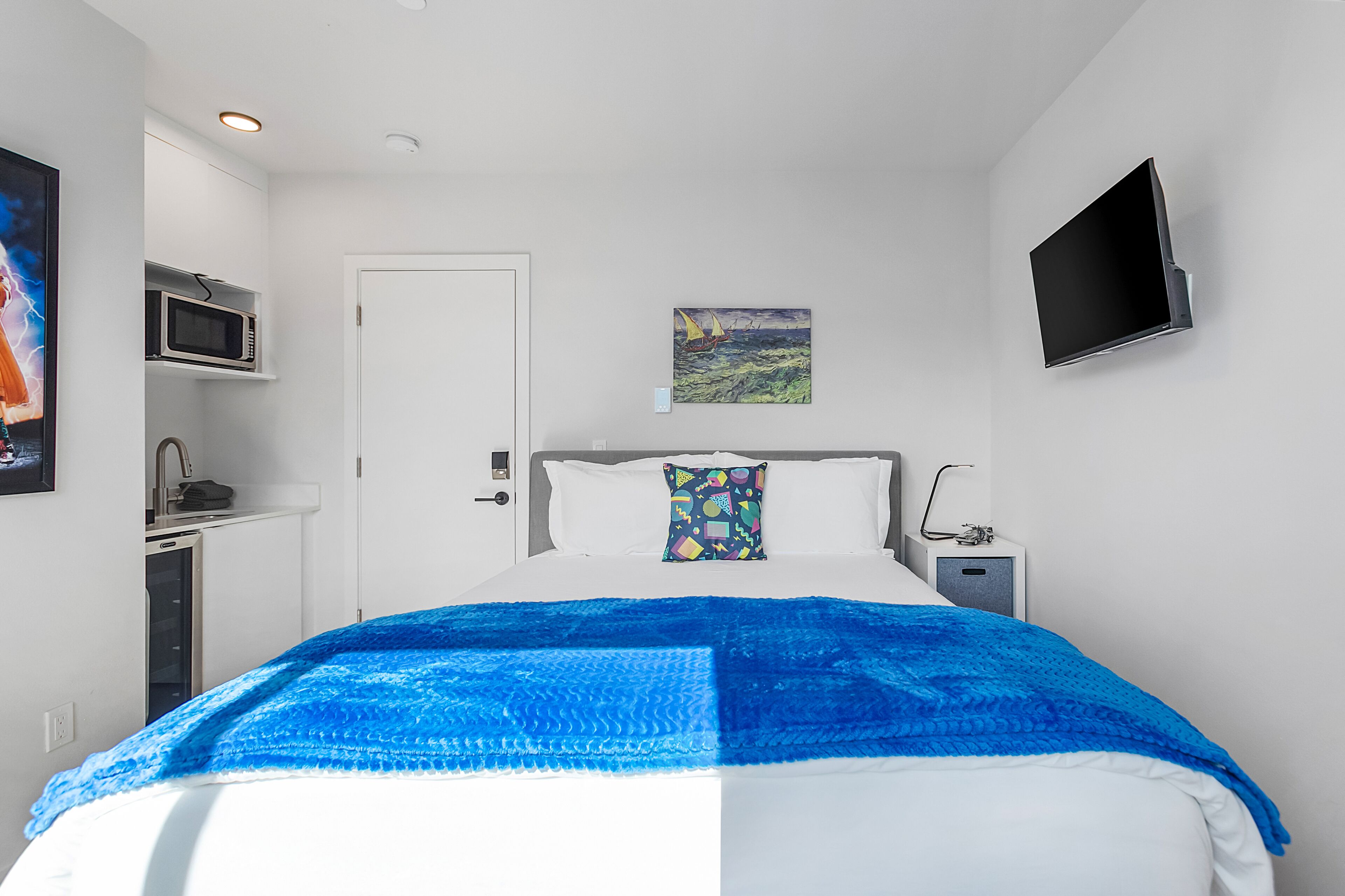 A hotel room with a bed, a flat-screen TV, a painting, and a microwave.
