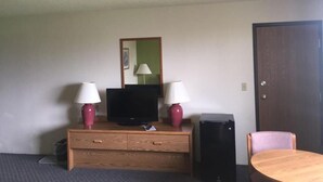A hotel room with a wooden dresser, two lamps, a television, a small black speaker, and a round wooden table. - Prairie Rose inn   (Edgeley)