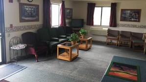A living room with a sofa, armchairs, a coffee table, and a TV. There are two windows with curtains, a clock on the wall, and a framed picture. - Prairie Rose inn   (Edgeley)