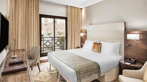 A hotel room with a bed, a desk, a chair, a TV, and a view of a building through a window. - Copthorne Makkah Al Naseem (Makkah)