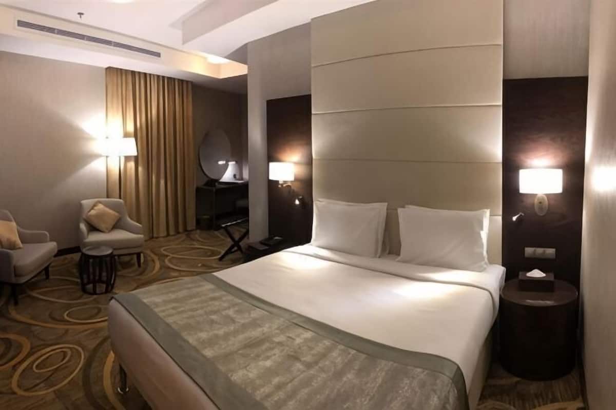 A hotel room with a large bed, two bedside lamps, a chair, a desk, and a mirror.