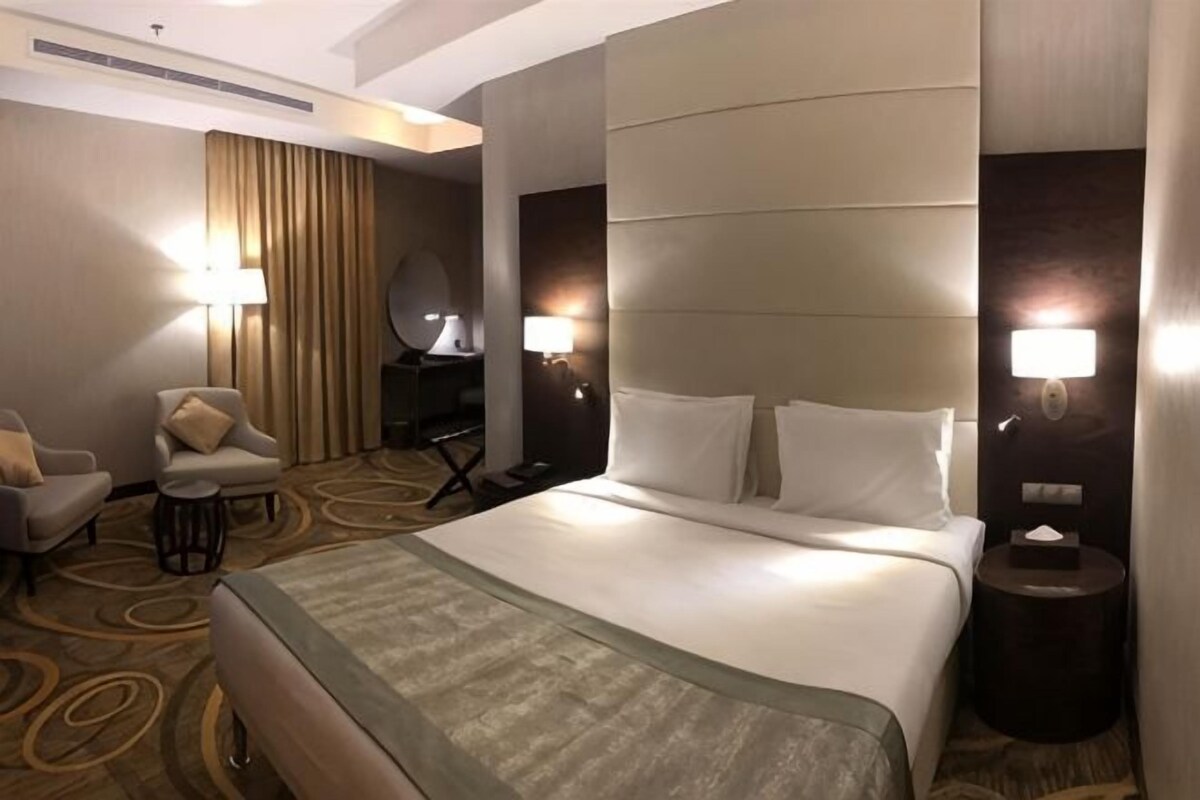 Una habitación de hotel con una cama grande, dos lámparas de noche, una silla, un escritorio y un espejo.