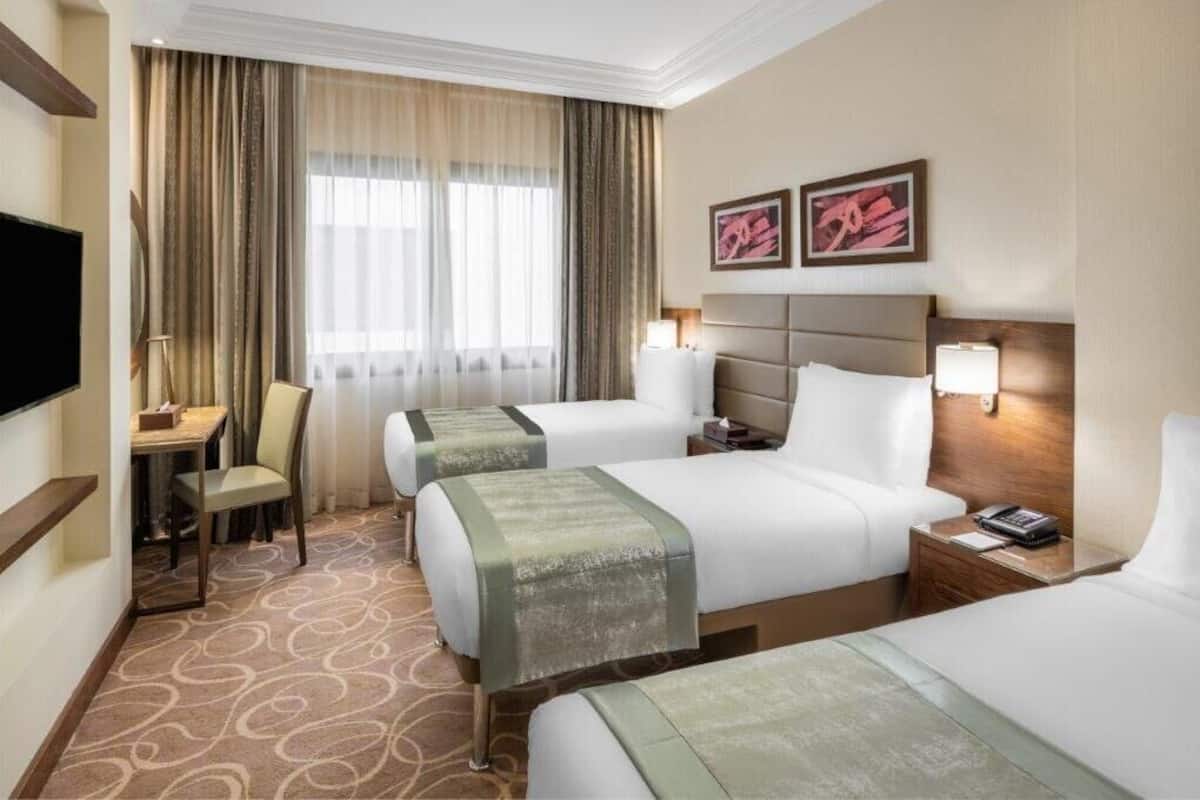 A hotel room with two beds, a desk, a chair, a TV, and artwork on the wall.