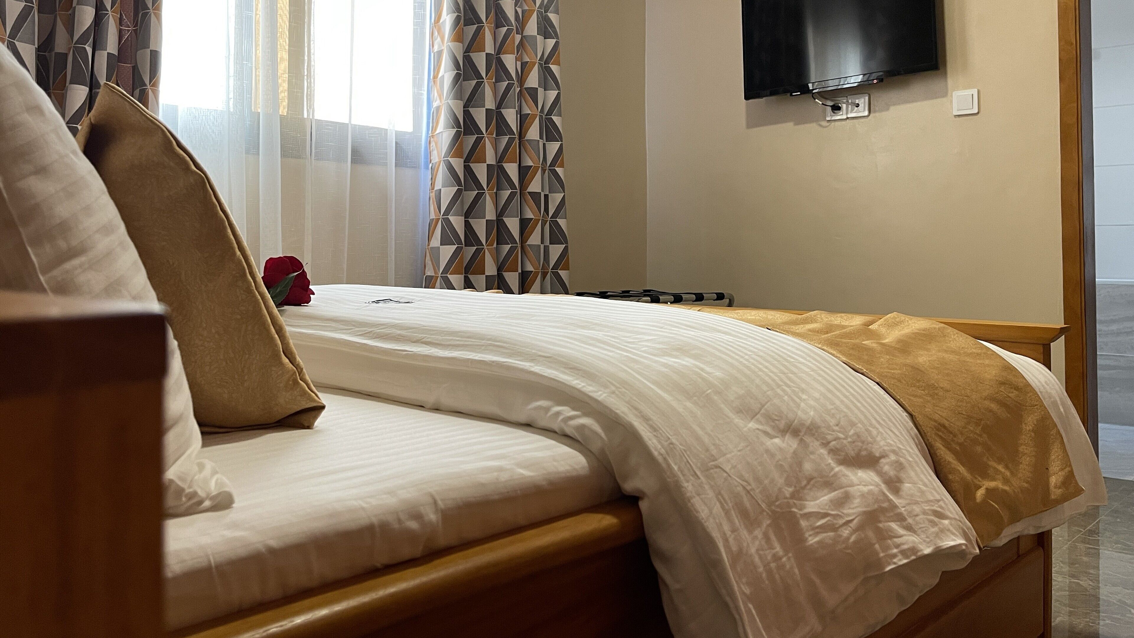 A hotel room with a bed, a TV mounted on the wall, and a window with curtains.
