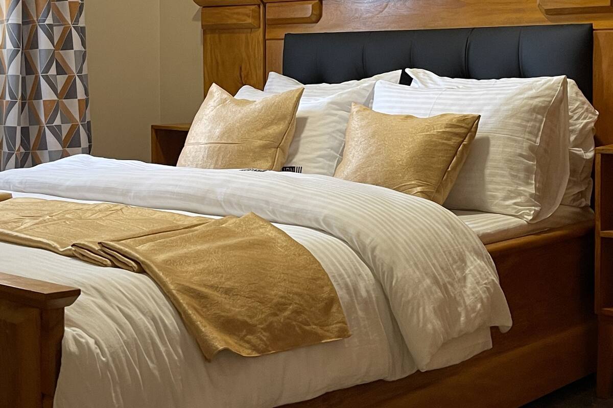 A neatly made bed with white and beige linens, a wooden headboard, and a bedside table with a lamp.