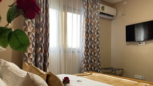 A hotel room with a bed, a TV mounted on the wall, and a window with patterned curtains. - JPN SQUARE Douala (Douala)