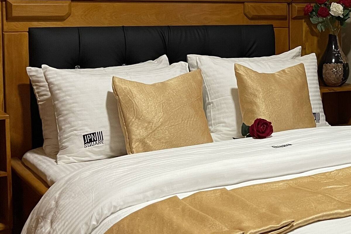 A neatly made bed with white and gold bedding, a black headboard, and a vase with flowers on the nightstand.