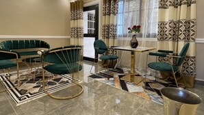 A room with a green sofa set, a small round table, and a vase with flowers. - JPN SQUARE Douala (Douala)