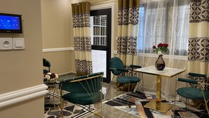 A dining area with a table and chairs, patterned curtains, and a vase with flowers. - JPN SQUARE Douala (Douala)