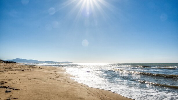 Ein Strand mit blauem Himmel und strahlender Sonne.