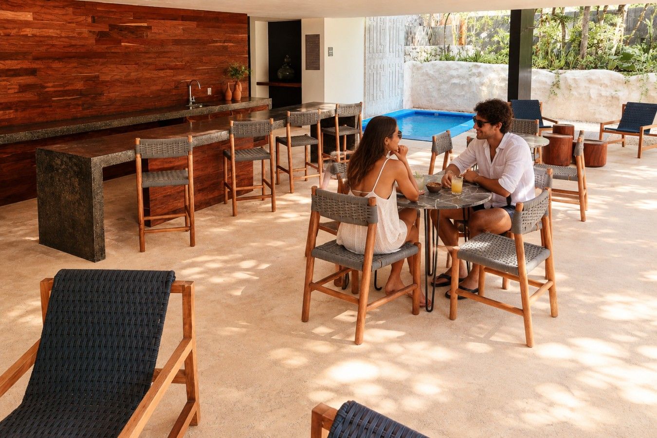 Ein Außenbereich mit Sitzgelegenheiten, einer Bar, Korbstühlen und einem Pool im Hintergrund.