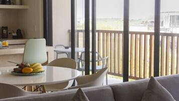 A modern living room with a grey sofa, a dining table with fruit, and a balcony with a wooden railing.