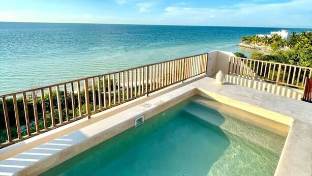 Una piscina con vista despejada al océano, rodeada por una cerca blanca y un balcón.