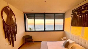 Un dormitorio con una cama grande, vista al mar a través de una ventana y un tapiz de macramé en la pared.