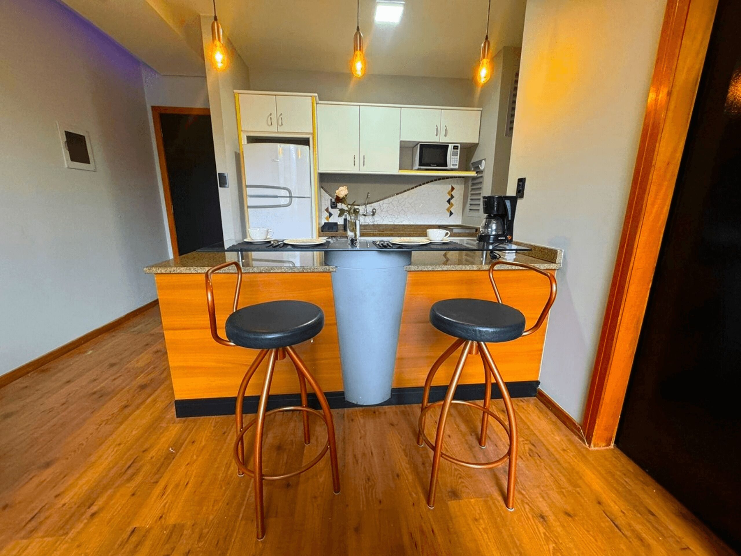 Una cocina compacta con una isla central, dos taburetes de bar, un microondas y una cafetera.