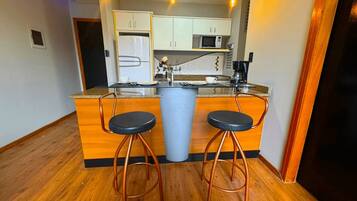 A compact kitchen with a central island, two bar stools, a microwave, and a coffee maker.