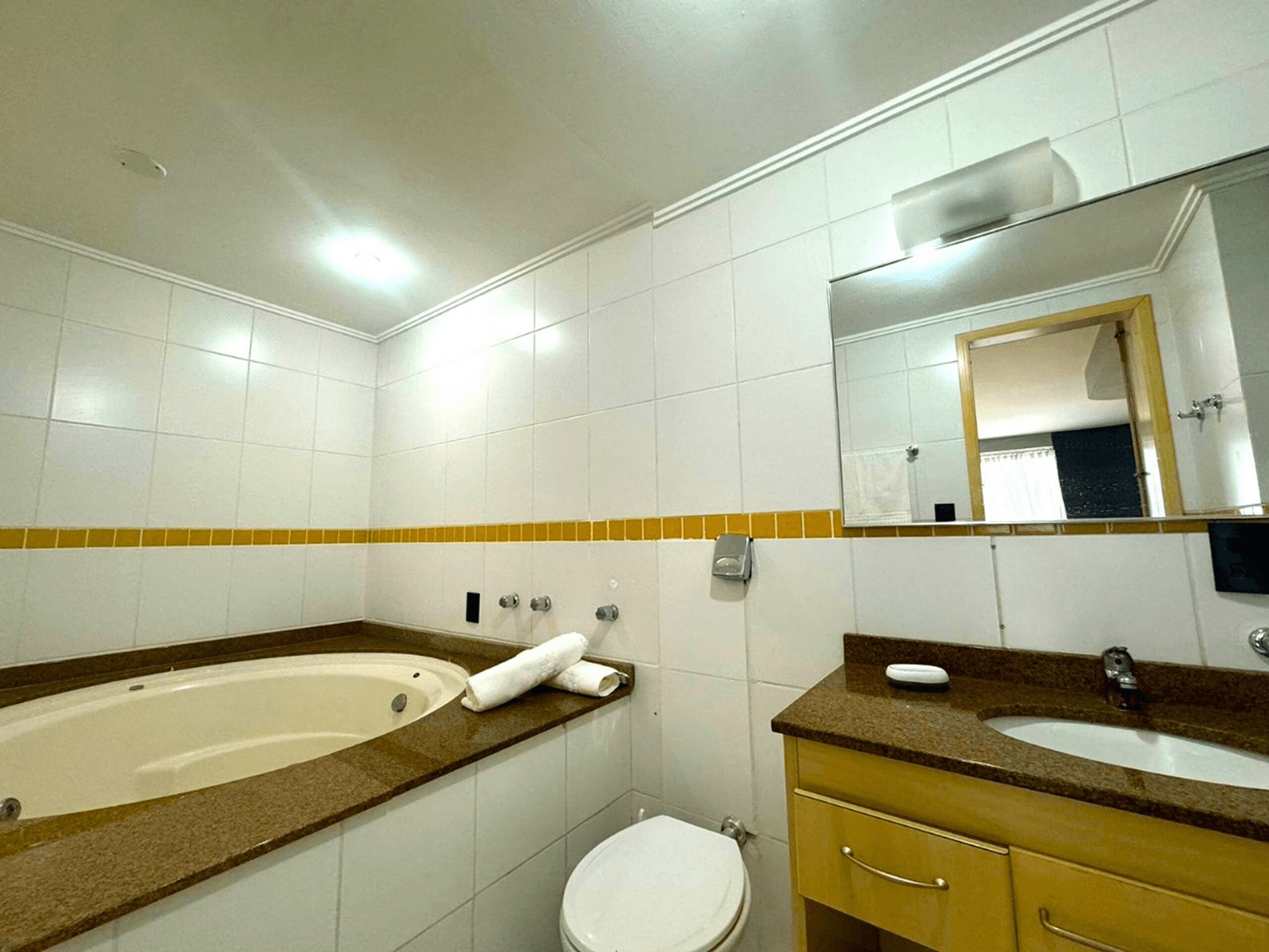 Une salle de bain avec des carreaux blancs, une baignoire, des toilettes, un lavabo et un miroir.
