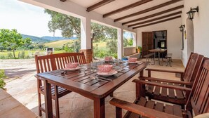 A wooden table set for dining with chairs, a stone floor, and a view of a green landscape.