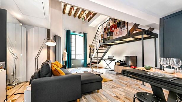 A modern living space with a sofa, dining table, and a staircase leading to a loft area.