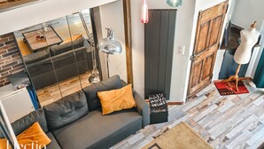 A modern living room with a grey sofa, orange cushions, a hanging lamp, and a wooden door.