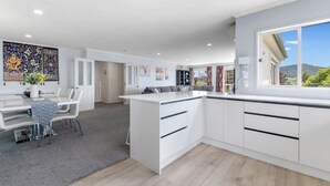 A modern kitchen with white cabinetry, a dining area with a table and chairs, and a large window offering a view of the outdoors. - Lakeview Mountain-view 3BR Home close to Rotorua Centre (Rotorua)