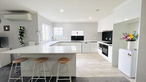 A modern kitchen with a large island, bar stools, a dishwasher, and a refrigerator. - Lakeview Mountain-view 3BR Home close to Rotorua Centre (Rotorua)