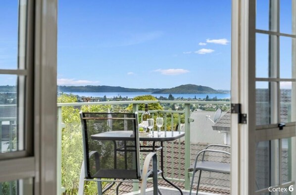 En balkon med et bord og stole, der giver udsigt over et smukt landskab med bakker og et vandområde.