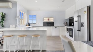 A modern kitchen with white cabinetry, a stainless steel refrigerator, and a large island with stools. - Lakeview Mountain-view 3BR Home close to Rotorua Centre (Rotorua)
