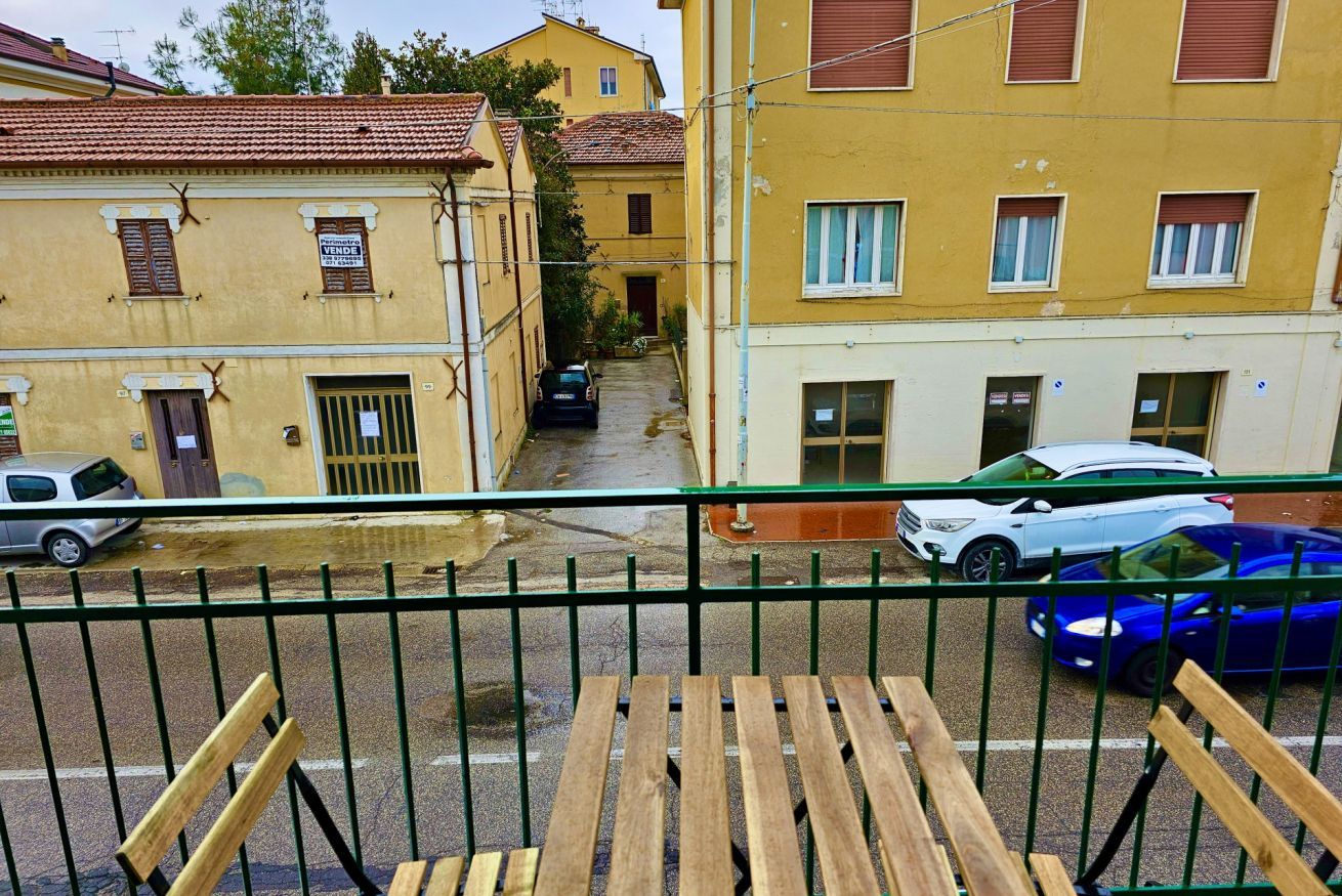 Un balcon donnant sur une rue étroite bordée de bâtiments jaunes, avec une voiture garée et une voiture bleue.