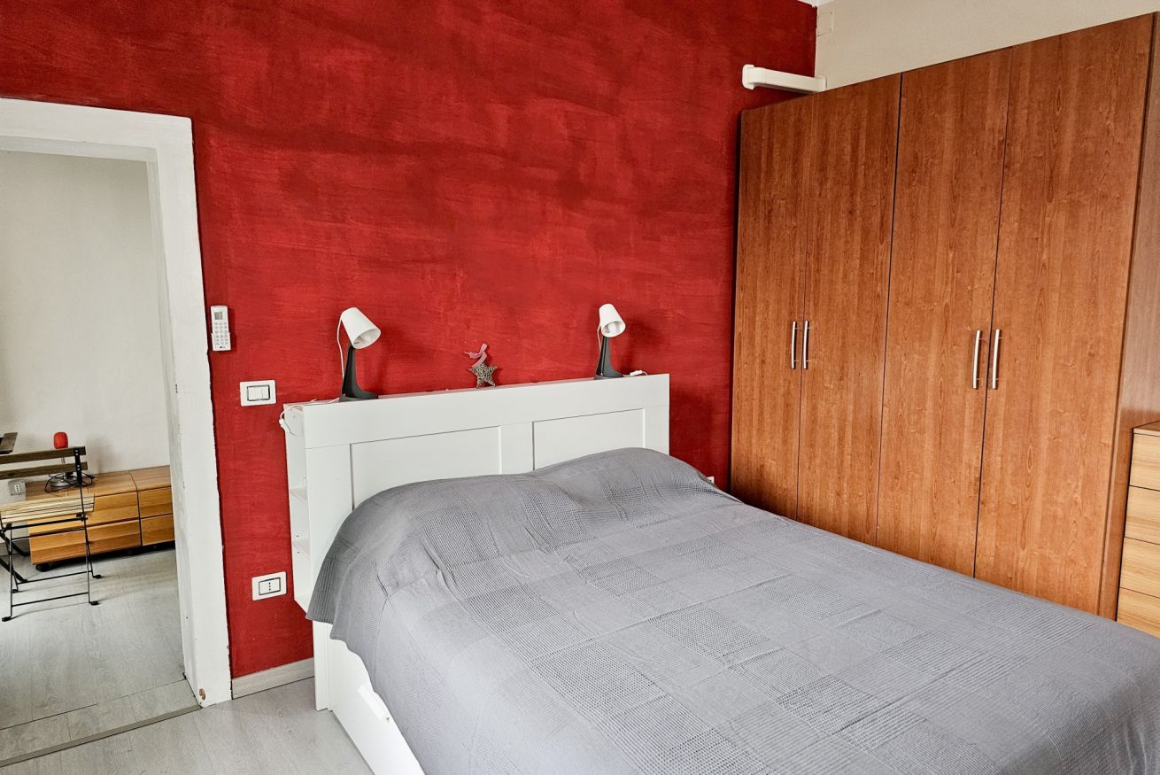 Camera da letto con un letto, una parete rossa, un armadio in legno e una testiera bianca.