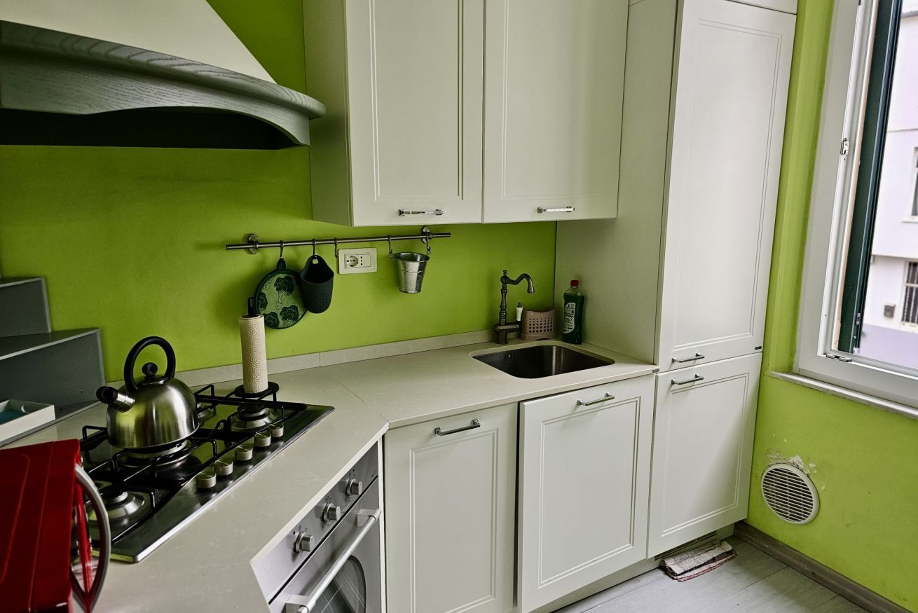 Cucina con piano cottura a gas, bollitore, lavello e mobili bianchi.