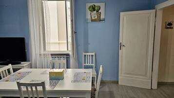 Una habitación con una mesa de comedor, sillas, un televisor, una ventana con cortinas, una puerta y un cuadro colgado en la pared.