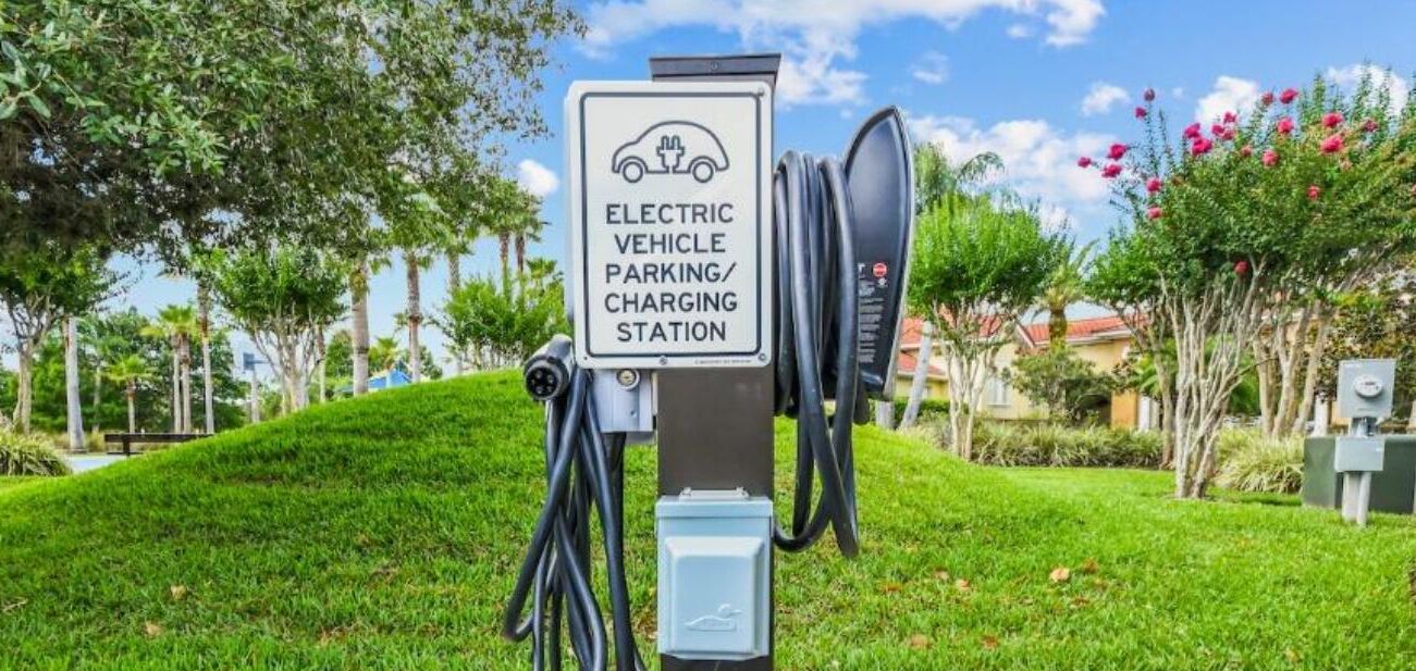 An electric vehicle parking and charging station in a landscaped area with trees and grass.