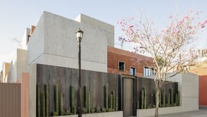 Um edifício moderno com fachada de concreto, portão de metal e um jardim de cactos.