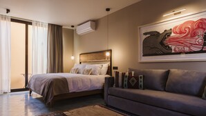 Quarto de hotel moderno com uma cama, um sofá, uma mesa de centro e uma grande obra de arte na parede.