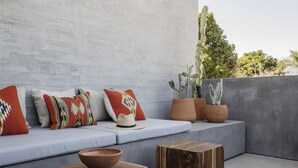 Uma área de estar moderna ao ar livre com parede de concreto, uma planta cacto e uma mesa de madeira com uma tigela.