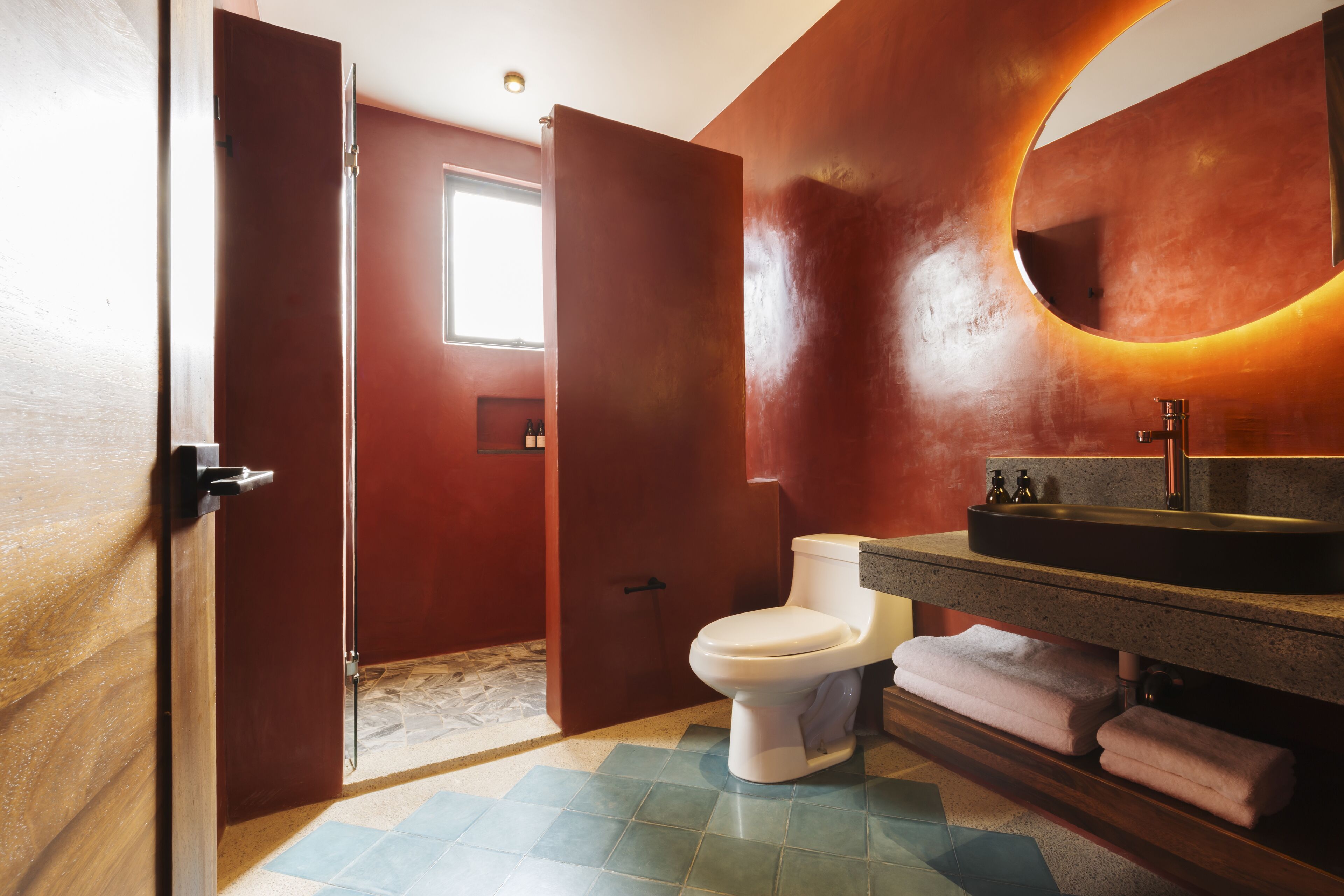 Ein Badezimmer mit Toilette, Waschbecken und einem Spiegel mit runder Beleuchtung.