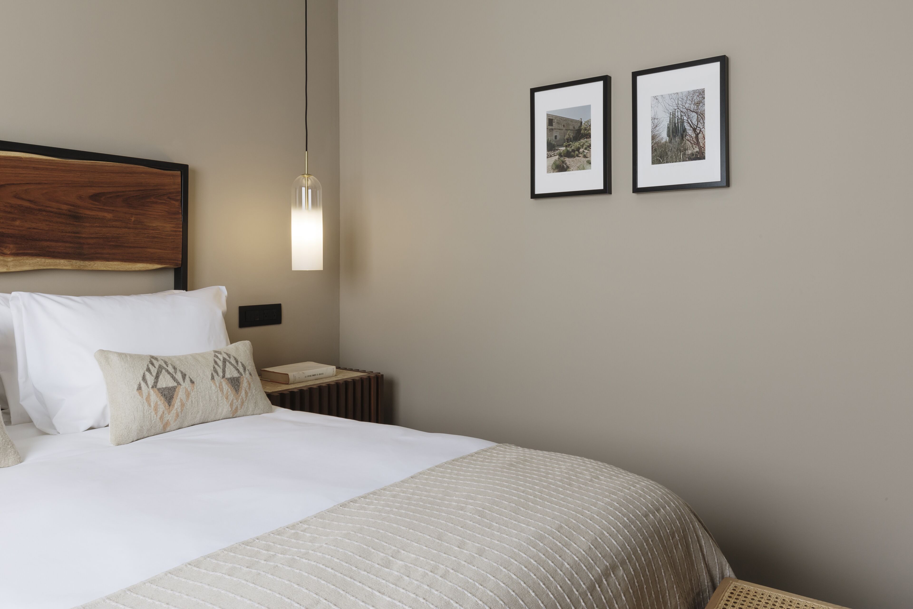 A neatly made bed with a wooden headboard, a bedside lamp, and two framed pictures on the wall.